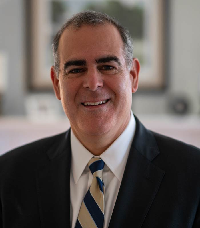 Headshot of Richard Milone wearing black blazer and gold-and-blue tie