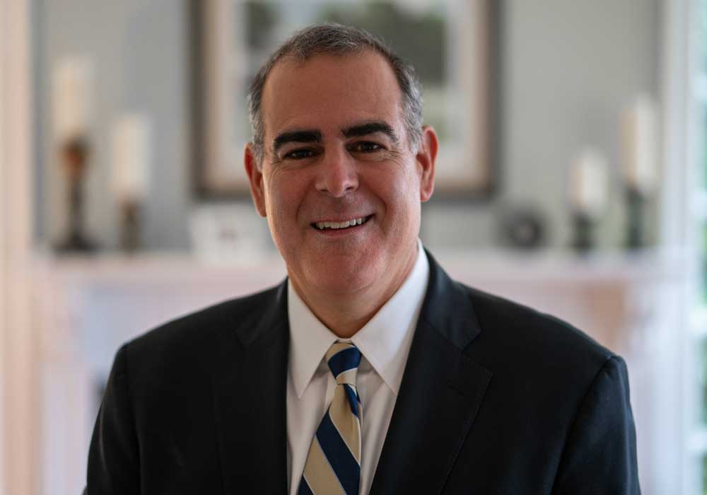 Headshot of Richard Milone wearing black blazer and gold-and-blue tie