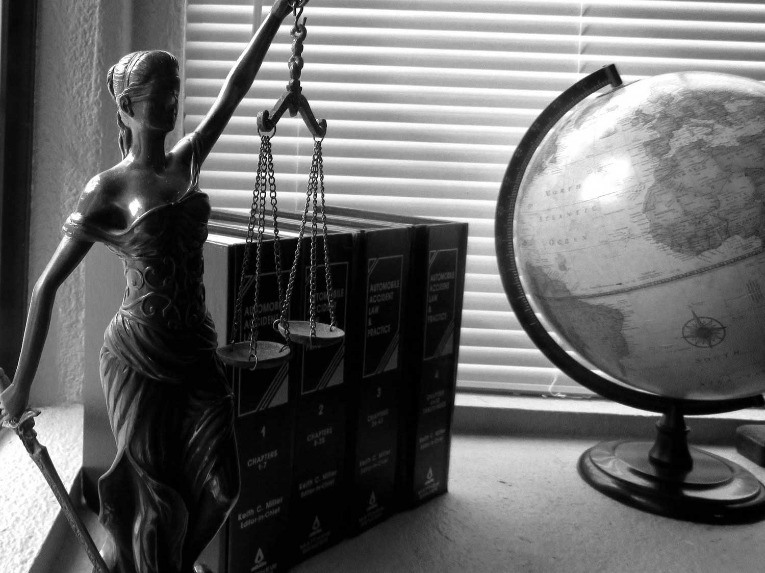 Black-and-white photo of Lady Justice figure in front of 4 law books next to a globe