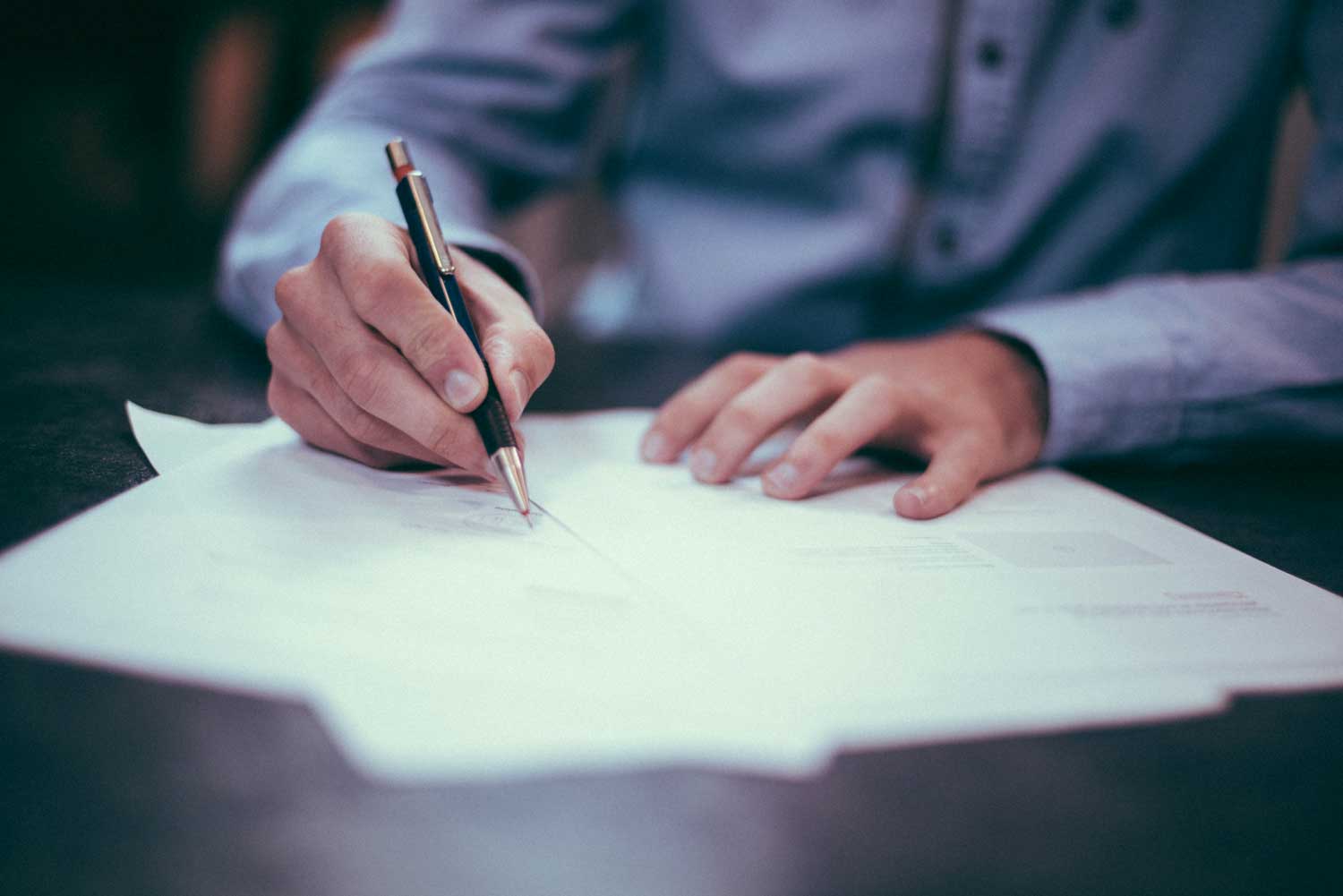 Person wearing long-sleeved blue dress shirt is marking a document with a black-and-gold pen